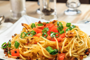 spaghetti with tomatoes, roasted garlic and green onions on a beautiful rectangular plate are on the table