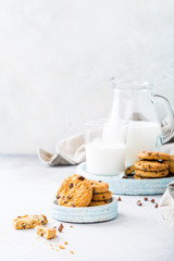 Stack of chocolate chip cookies on blue stone plate with glass of milk on light gray background. Selective focus. Copy space.