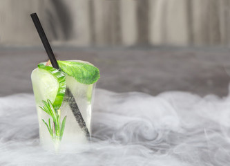 glass with fresh cocktail made of ice in vapour on concrete table