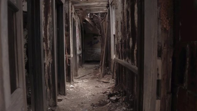 FPV CLOSE UP: Exploring decaying abandoned building with crumbling walls and collapsing ceilings. Walking along the dark narrow corridor past creepy dark rooms in ruined disintegrating dangerous house