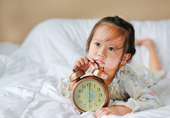 Cute little girl with alarm clock lying on bed.