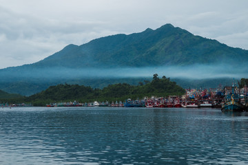 beautiful blue sea, fisherman village on coast and have big mountain, fog are bacgkround. this image for landscape,seascape and nature concept