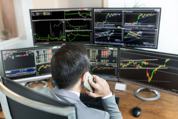 Over the shoulder view of and stock broker trading online while accepting orders by phone. Multiple...
