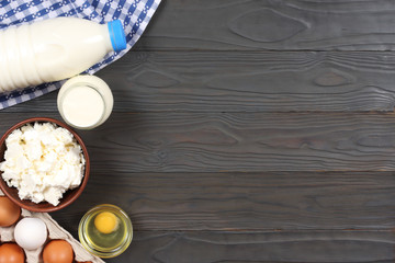 Glass jug pitcher of fresh milk with glass, eggs and cottage cheese in a rustic setting on the wooden background  with copy space. Top view.