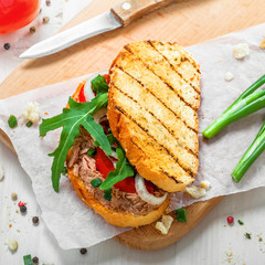Toast sandwich with tuna, tomato, onion and arugula. Traditional healthy food made of fish, vegetables and grilled bread. Top view.