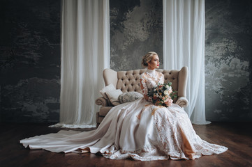 Beautiful bride in a cream wedding dress with a wedding bouquet, with orange and white flowers. Studio, gray background, modern, sofa, lace dress.
 - Powered by Adobe
