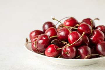  Fresh berries. Ripe sweet cherry on a white plate on a light background.