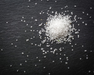 A bunch of white salt crystals on a black stone background. Seasoning for eating. Scattered over the surface.