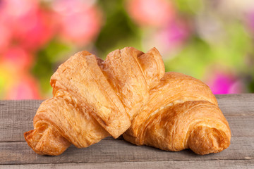 two croissant on a wooden board with a blurry garden background