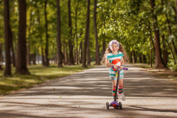 Fototapeta premium Little girl learn to ride scooter in a park on sunny summer day.