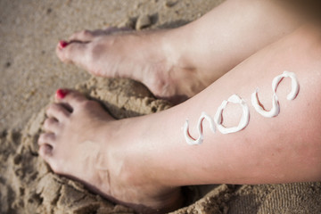 Sunscreen sun drawing lotion on suntan legs relaxing tanning on tropical beach holiday. Women lower body lying with sunblock cream in shape for skin cancer sunburn care concept.
