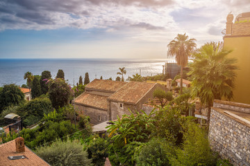 Fototapeta na wymiar Taormina, Sicily - Beautiful view of the famous hilltop town of Taormina with palm tree, mediterranean sea and sunshine