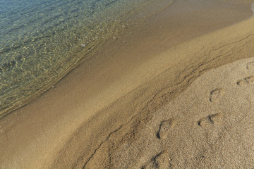 Soft sea wave on sandy beach, Beautiful Greek beach with fine sand and footsteps, Close up photo of sandy beach with soft wave in motion