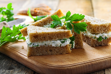 Sandwiches made of rye bread, cream cheese, green onion and fresh parsley on a rustic table. Delicious healthy appetizers. Close-up shot.