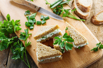 Healthy simple snack made of rye bread, cream cheese, fresh parsley and green onion on a table. Delicious small sandwiches. Top view.