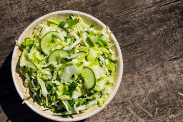 Spring vegan salad with cabbage, cucumber, green onion and parsley on wooden table