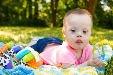 Portrait of Cute baby boy with Down syndrome lying on blanket in summer day on nature