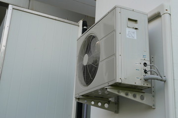 Air conditioner condenser unit at a  white concrete wall