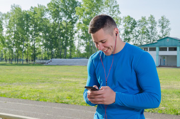 A young athlete writes a message on the smartphone after training and listens to music