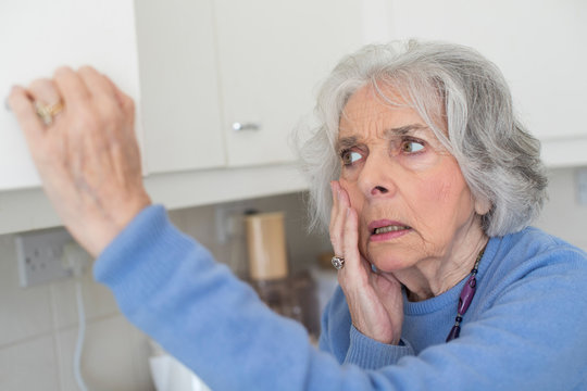 Forgetful Senior Woman With Dementia Looking In Cupboard