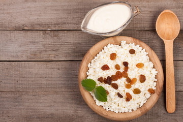 Cottage cheese in bowl with sour cream and raisins on old wooden background with copy space for your text. Top view