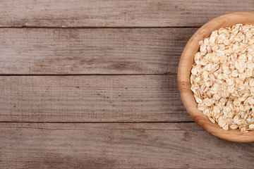 Oat flakes in a wooden bowl on old wooden background with copy space for your text. Top view