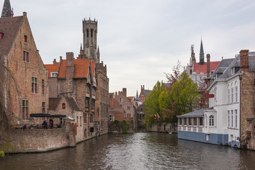 Old town of Bruges (Brugge) with brick houses and small restaurants above canal and famous Belfry on the background, Belgium