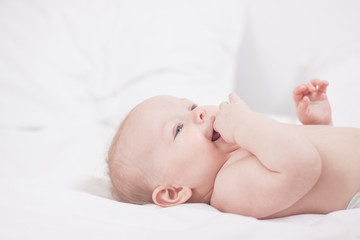 portrait of Cute baby with fingers in mouth in white bed