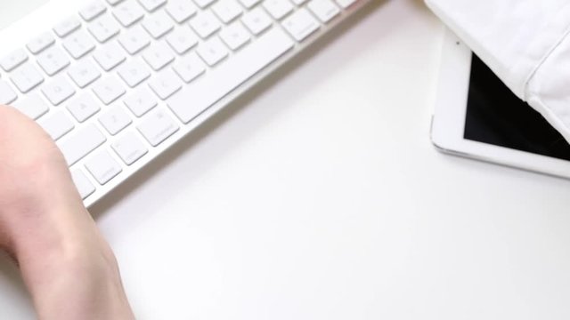Female hands are laying out a keyboard, a tablet and a notebook on the white table