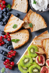 Variety of ingredients for making dessert sandwiches with bread, berries and cream cheese. Red currant, blueberries, sliced kiwi, figs over gray metal background. Flat lay, summer appetizer concept