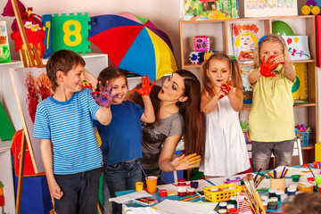 Small students with teacher finger painting in art school class. Teacher cheers children in kindergarten. Craft education develops creative abilities . Kids are fond of painting pictures with palms.