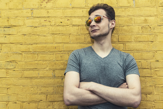 Pretty handsome confident young man hipster with sunglasses smiling behind yellow wall. Looking aside. Horizontal.
