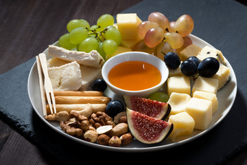 plate of cheeses, snacks and fruits on a dark background