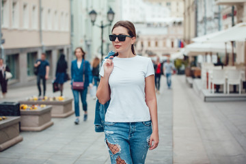Obraz na płótnie Canvas Attractive girl in sunglasses walking along the street. White t-shirt. Mock-up.