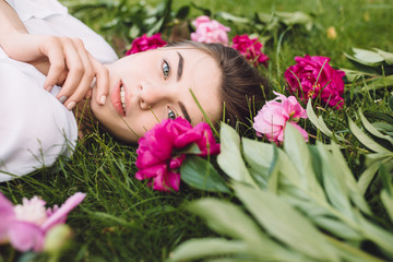 Obraz na płótnie Canvas Woman lying on grass with flowers peonies around
