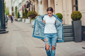 Attractive girl in a jeans jacket and white t-shirt walking along the street. Mock-up.