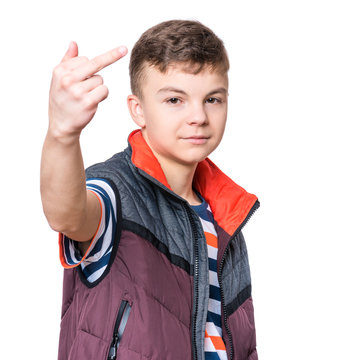 Emotional portrait of irritated teen boy - isolated on white background. Furious teenager looking with anger at camera and show middle finger or fuck you sign.
