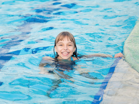 Close-up portrait of happy girl in the swimming pool at aquapark. Cute child having fun enjoyable time on vacation. Looking at camera.