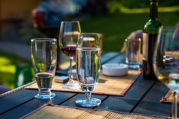 Glasses of wine, bottle, water on garden table, outdoor.