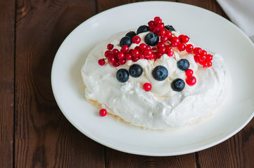 Close up of homemade individual meringue cakes Pavlova with whipped cream with mascarpone fresh blueberries and red currants in a white plate on a white stone background. Copy space.