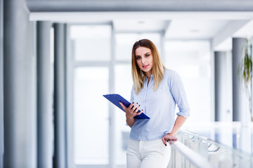 Beautiful business woman standing and looking straight while holding paper board