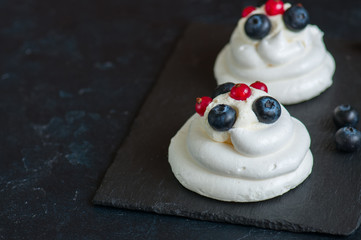 Close up of homemade individual meringue cakes Pavlova with mascarpone whipped cream decorated with fresh blueberries and red currants on a gray stone background. Copy space.