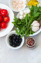 Ingredients for healthy salad. Tomatoes, arugula, onion, mozzarella, olives, garlic and pepper with olive oil on a white stone background. Vegetarian food, health or cooking concept.