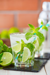 Two fresh mojitos cocktail in glass on wooden table. Mojitos with mint leaves, lime and ice. Drink making tools and ingredients for cocktail. 
