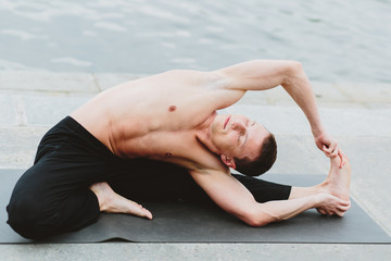 a young man practicing yoga asanas in the city on the waterfront