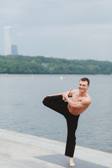 a young man practicing yoga asanas in the city on the waterfront