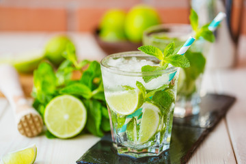 Two fresh mojitos cocktail in glass on wooden table. Mojitos with mint leaves, lime and ice. Drink making tools and ingredients for cocktail. 