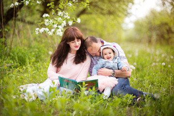 Mother and father reading a book with tales  to little daughter outdoors in the garden or the park