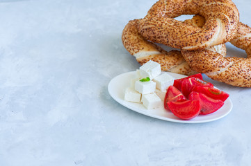 Traditional Turkish bagel (bread) - simit with tomatoes and feta cheese on a plate on a white stone background. Copy space and close up.
