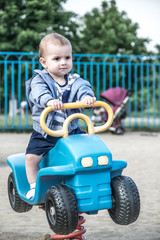 A cute baby boy driving a big toy car on a summer playground